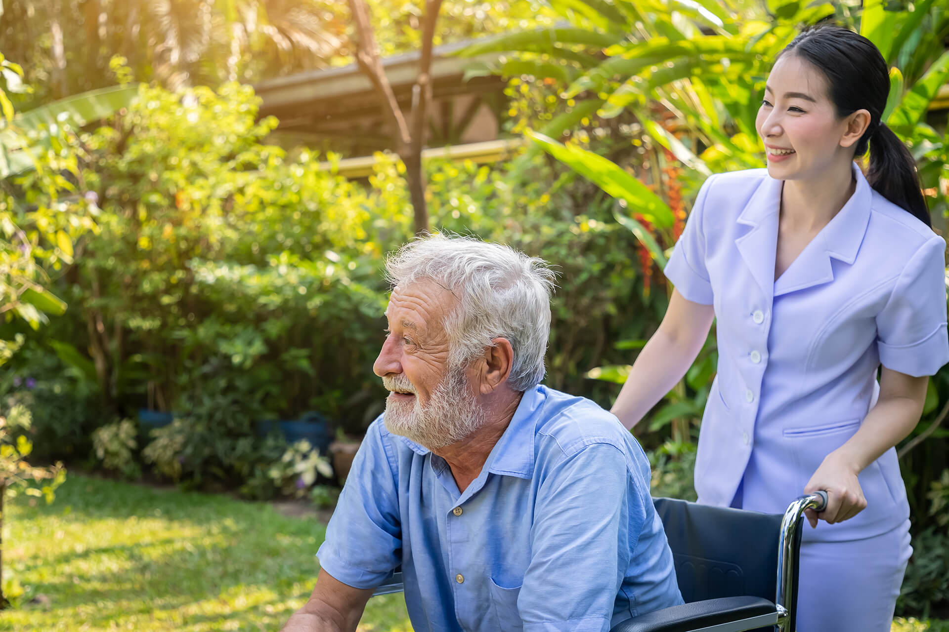 A smiling caregiver assists a happy senior man in a wheelchair outdoors, representing compassionate in-home and companion care services from Sunshine Home Care Services in Florida.