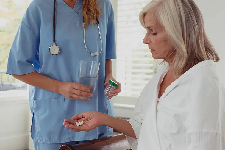 Medication Support and Personal Care at Home Caregiver providing senior woman with medication and water